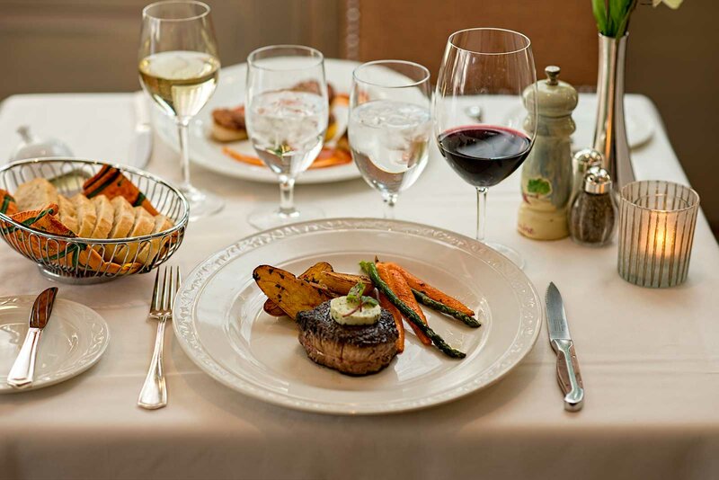 Set table with focus on steak entree with side or red wine